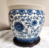 Full view of the large ceramic planter with blue botanical patterns on white glaze, sitting on the carved wood base.
