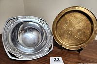 Photo showing the Lenox metal bowl with decorative cutouts and the vintage brass plate with symbolic engravings side by side.