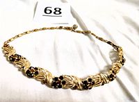 Full view of signed Lisner gold tone choker necklace with topaz rhinestone floral design laying flat on white background.