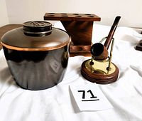 Photo of wood pipe rack, black metal container with lid, pipe on brass and wood holder