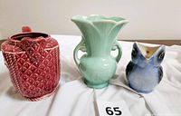 Front view of three pottery items: blue bird-shaped pitcher, green McCoy vase with double handles, and red square-bodied floral pitcher.