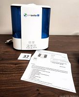 White and blue Pure Guardian ultrasonic humidifier with control panel and buttons on front and power cord visible. Product papers beside it.