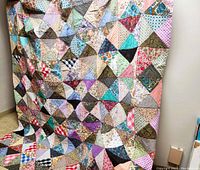 Full view of the colorful patchwork quilt hanging, showing overall pattern of triangle blocks in diverse pastel and muted colors.