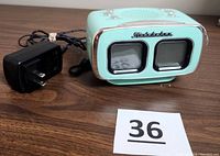 Front view of teal green Studebaker retro alarm clock radio showing dual display windows and power cord.