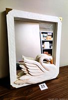 Full front view of white textured wood framed mirror with brass corner accents and large carved wooden swan figure attached to lower right corner.