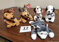 Front view of five Ty Beanie Babies dog plush toys sitting and lying on a wooden table, showing tags and details