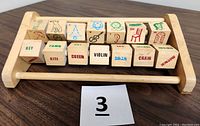 Top view of 14 four-sided wooden spinning blocks on wooden holder. Letters, words, and pictures visible (e.g., key, kite, queen, violin)