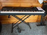 Front view of Alesis Recital Pro keyboard on X-style stand with sustain pedal and power adapter