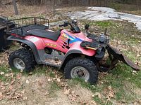 Left side view of red ATV showing front plow blade, winch, and rear cargo rack.