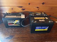 Two black plastic batteries on wooden surface with cables attached