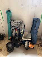 Shows the overall camping lot with cooler, lantern, umbrellas, kettle, pot, thermos, spray cans, folded tent or tarp, and carrying cases.