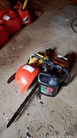 Full lot showing two chainsaws, work helmet, and oil container on concrete floor.