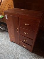 Front view of the wooden child's dresser, showing the closed wardrobe door on the left and four drawers on the right, with visible surface wear.