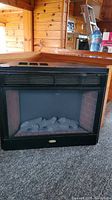 Front view of Coleman electric fireplace showing glass front and faux logs inside.