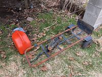 Side angle view of hand cart showing rusty metal frame, tires, and red plastic jerry can.