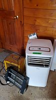 Wide view of two Koolking portable air conditioners and two portable heaters on the floor next to a wood door.