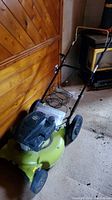 Green Radley push lawn mower with black 144cc engine cover in a wooden indoor setting.