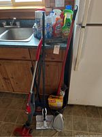 Photo showing upright vacuum, broom, mop, iron, dustpan, and cleaning products on kitchen counter.