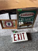 Three signs: Labatt's On Draft mirror, Molson Export mirror, Electric EXIT sign with cord on carpeted floor.