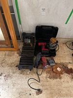 Wide angle view of all tools laid out on a dirty floor showing drill, sander, drill bits, handheld tool, and cases