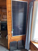 Motomaster Eliminator solar panel mounted vertically on a wooden wall, with two other panels on the floor.