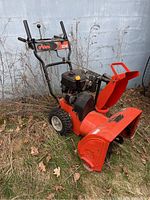 Full front-left view of snowblower showing red housing, chute, black engine and control handles