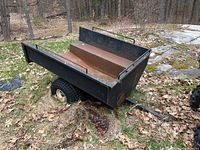 Front three-quarter view of steel trailer bed on two tires in wooded yard