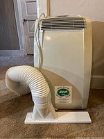 Side view of portable air conditioner showing exhaust hose and window venting panel on carpet.