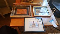 Top down photo of three framed Asian artworks with folded parasol behind on wooden table