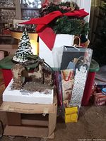 Photo showing nativity stable with partially destroyed rustic appearance, figurines packed in foam, gift bags, plush toys, and wreaths on a table
