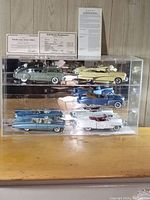 Frontal shot of clear acrylic display case showing six model cars on three shelves