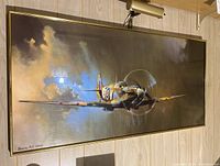 Framed controversial style fighter plane poster with attached overhead light fixture displayed on floor