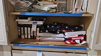 Flags folded and stacked on a shelf, including American flags and other fabric flags