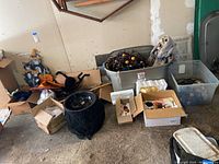 Overview photo showing multiple Halloween decorations including storage totes and boxes with various holiday-themed items, skeleton, and large black cat figure.