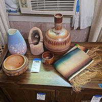 Lot of five pottery pieces and one woven blanket arranged on wooden surface beneath an air conditioner unit.