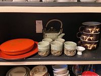 Ceramic tea pot, four light green crackle glaze cups, two orange oval dishes with lids, three brown cups stacked