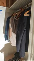 Side view of various men's vintage jackets, including suit jackets and darker overcoats hung on wooden hangers in a closet