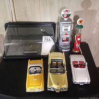 Full lot showing two model cars, display case, and two gas pump models arranged on a black surface.