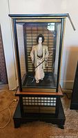 Full view of Japanese samurai doll in the glass display case with wooden base.