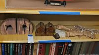 Shelf with sandstone hand-shaped bookends, petrified wood bookends, wrapped straw figures, and bead strands alongside books