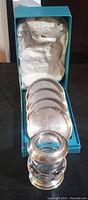 Set of four sterling silver round coasters inside blue box with crumpled white cushioning paper.