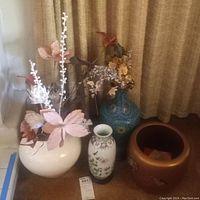 Front view of group: white ceramic vase with faux florals, small porcelain vase, blue cloisonne-style vase on stand, and gold planter pot
