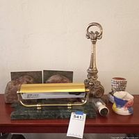 Photo showing vintage desk lamp with dark green marble base and brass curved shade alongside ornate brass and stone geode bookends paired in two sets, plus small clay and shell vessels grouped on wood table