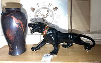 Photo showing black ceramic panther statue with jeweled collar and Asian style vase with bird motif side by side on a wooden surface.