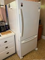 Full view of white Whirlpool refrigerator in kitchen, showing front and side profile, highlighting the top door and bottom freezer drawer.