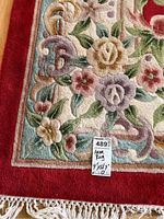 Corner close-up showing red field, pastel floral border and white fringe