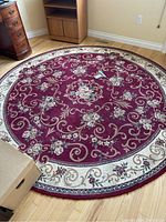 Full view of large round floral area rug with burgundy background and cream border showing floral and scroll pattern