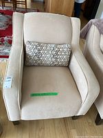 Front view of cream-colored fabric armchair with decorative pillow.