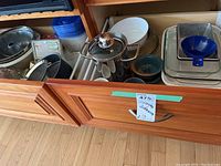 Two wooden drawers open displaying a variety of baking pans, bowls, a stainless steel pot with glass lid, and plastic containers.