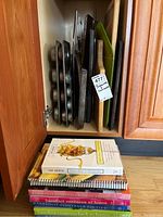 Contents of cabinet showing stacked metal baking trays including muffin pans, cutting boards in wood and plastic, with a label for listing identification